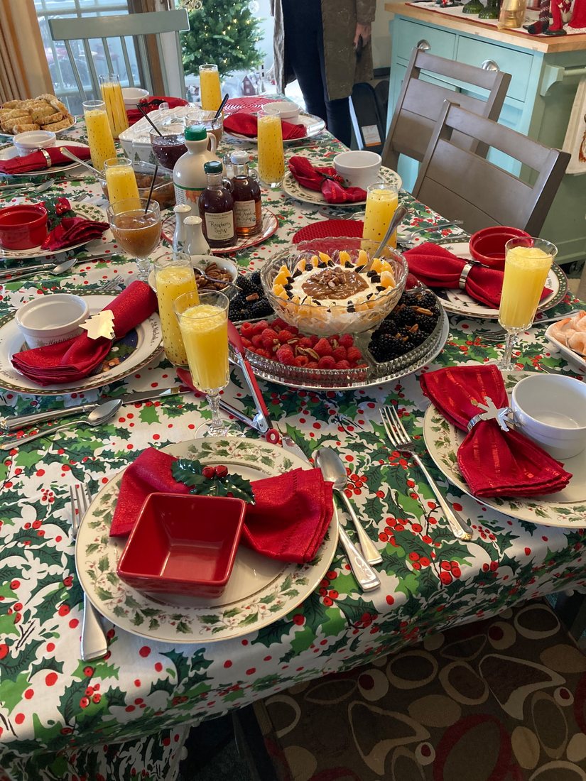 A holiday party table with holly-print cloth, tiered desserts and mimosas